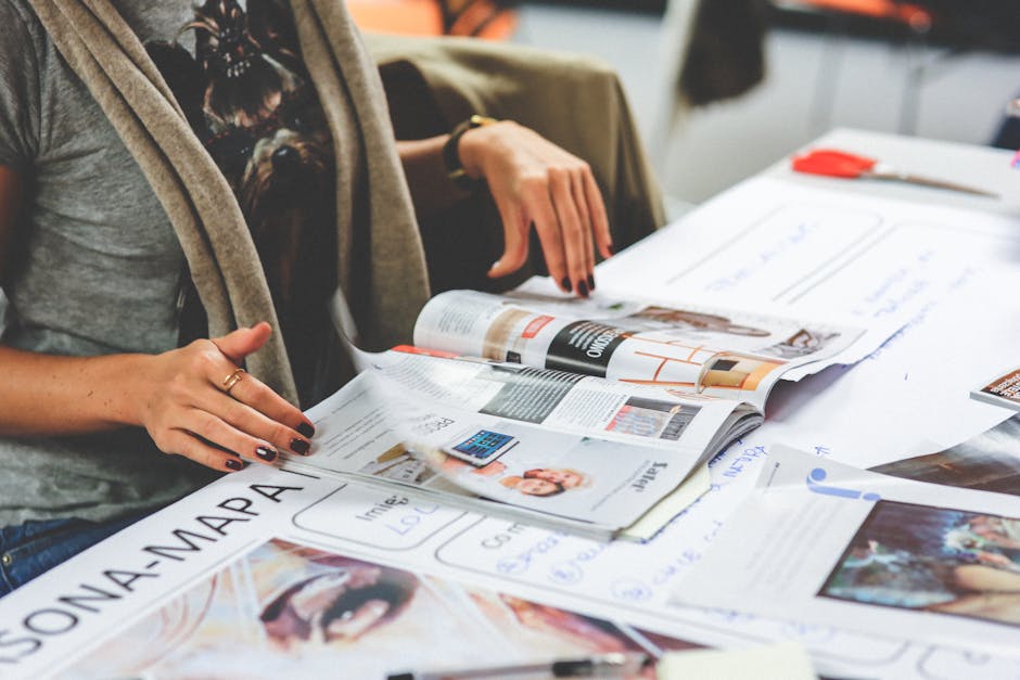 Detail shot of a woman browsing through magazines on a table filled with printed materials.