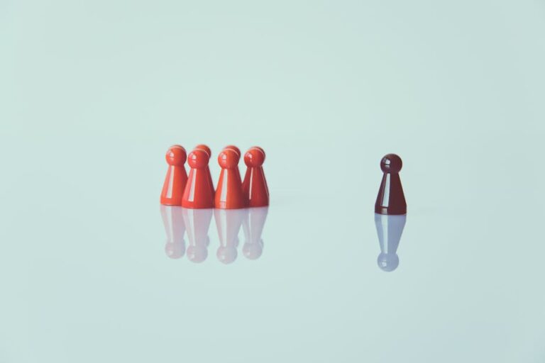 Red game pieces grouped with one isolated piece symbolizing social distancing on a reflective surface.