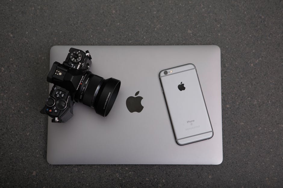 High-angle shot of DSLR camera, MacBook, and iPhone on textured surface, showcasing modern technology essentials.