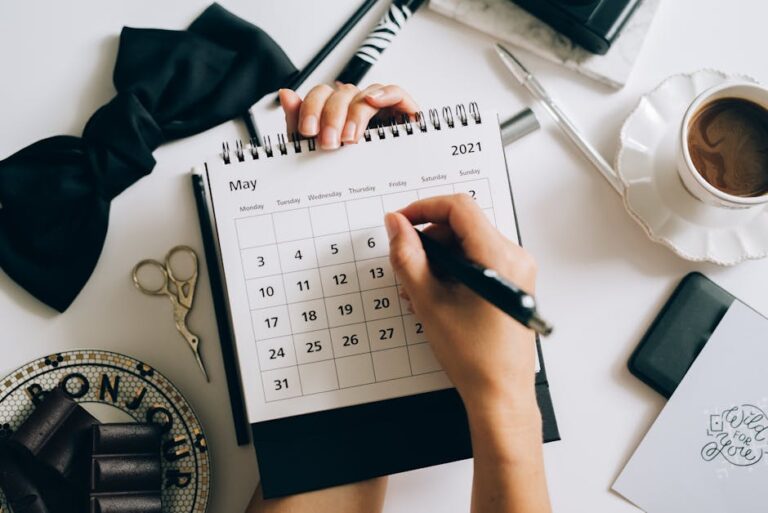 Top view of hands using a planner with coffee and accessories, focused on May 2021 calendar.